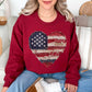 Model wearing a Gildan 18000 Sweatshirt in muted denim blue (washed denim) with a patriotic heart design made of red, white, and blue American flag patterns in a faux patchwork and stitched fabric style.