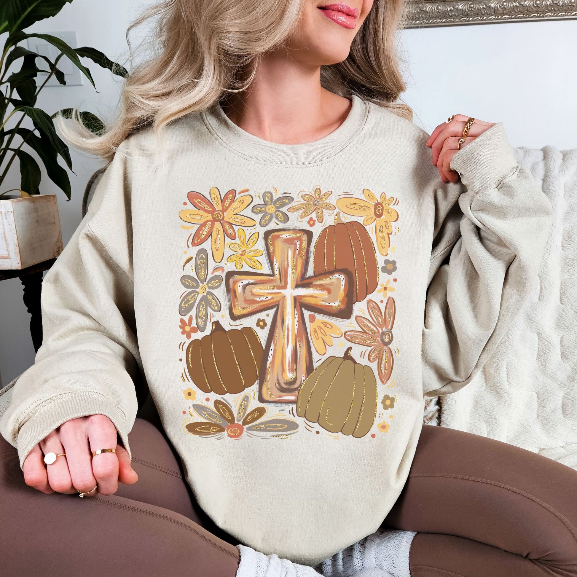 Model wearing a light beige (sand) featuring a hand-drawn style Christian cross surrounded by brown, rust and muted green pumpkins with whimsical autumn flowers in mustard, orange, brown and gray.