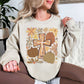 Model wearing a light beige (sand) featuring a hand-drawn style Christian cross surrounded by brown, rust and muted green pumpkins with whimsical autumn flowers in mustard, orange, brown and gray.