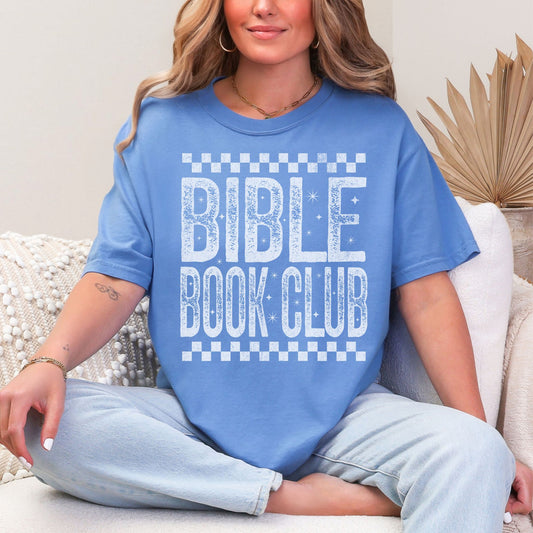 Model wearing a Comfort Colors 1717 T-Shirt in muted blue-green (mystic blue) featuring a distressed large word graphic that says, "Bible Book Club" Racer checkered stripes are on the top and bottom of the print.