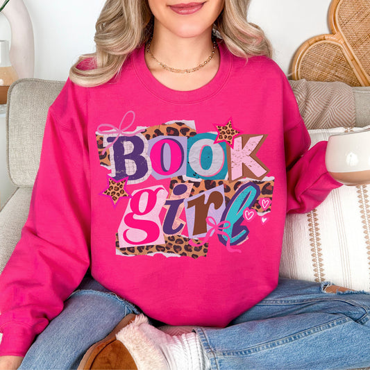 Model wearing a Gildan 18000 on bright pink (heliconia) featuring a colorful ‘Book Girl’ collage graphic with leopard print accents, stars, bows, and hearts.