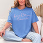 Model wearing a Comfort Colors 1717 t-shirt in a muted blue-green (mystic blue) color featuring a graphic design of a cursive script font that says "book lover" with a bow after book.