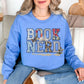 Model wearing a Gildan 18000 soft sky blue (carolina blue) Sweatshirt featuring the words “BOOK NERD” in large block letters filled with collage-style patterns including vintage book pages, florals, and textures, with an open book and small botanical accents incorporated into the design.