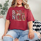 "Book Nerd" graphic on a muted brick red (chili) t-shirt.