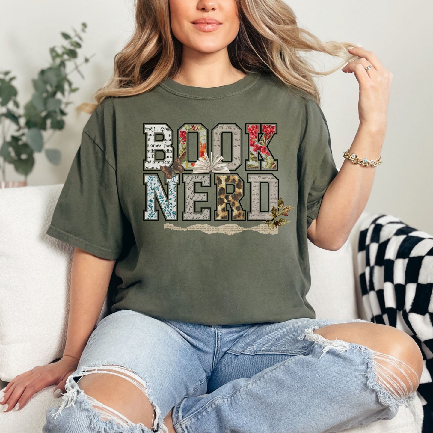 Model wearing a Comfort Colors 1717 Muted green (sage) T-shirt featuring the words “BOOK NERD” in large block letters filled with collage-style patterns including vintage book pages, florals, and textures, with an open book and small botanical accents incorporated into the design.