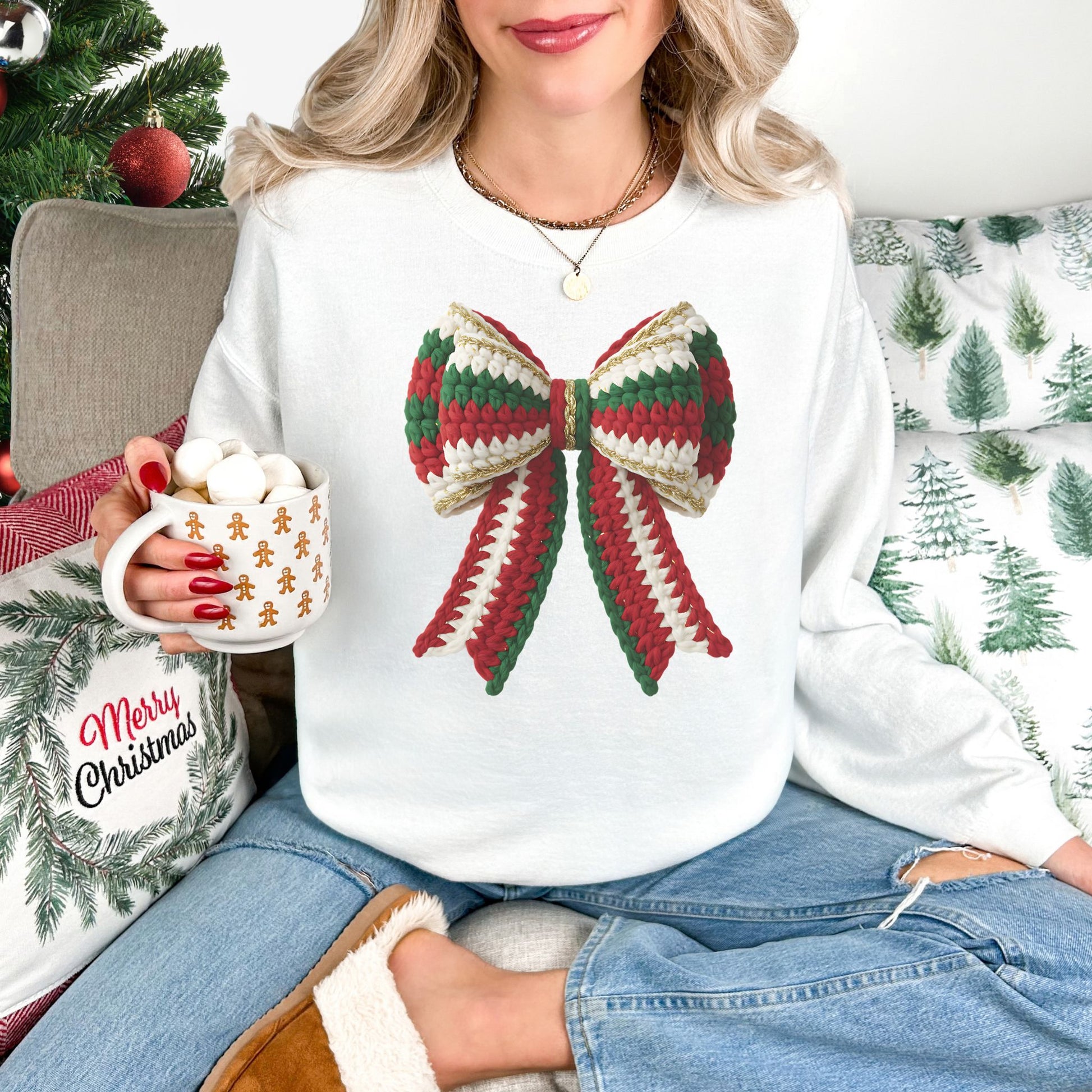 Model wearing a Gildan 18000 long-sleeve sweatshirt in white (White) featuring a large Christmas bow with red, green, and cream faux crochet stitches, gold-colored trim, and two long ribbon tails.