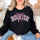 Model is wearing very black (black) Gildan 18000 Sweatshirt featuring the word “BOOKISH” in a soft pink varsity type lettering with a pink bow accent centered above the text.