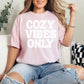 "Cozy vibes only" graphic on soft pink (blossom) T-shirt.