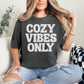 Model wearing a Comfort Colors 1717 on dark charcoal gray (pepper) featuring a graphic that says, "Cozy vibes only" in a large bubble font.
