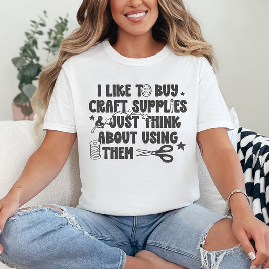 "I like to buy craft Supplies and just think about using them. graphic on a white shirt.