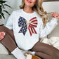 Model wearing a Gildan 18000 sweatshirt in bright white (white) featuring a faux crochet American flag bow design with stars and stripes in a handmade-inspired style.