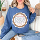 Model is wearing a Gildan 18000 rich medium-dark blue (indigo blue) Sweatshirt featuring a faux embroidery-style design of a wooden embroidery hoop with stitched lettering that reads “HOME BODY,” accented with small pink stitch details and a heart at the bottom.