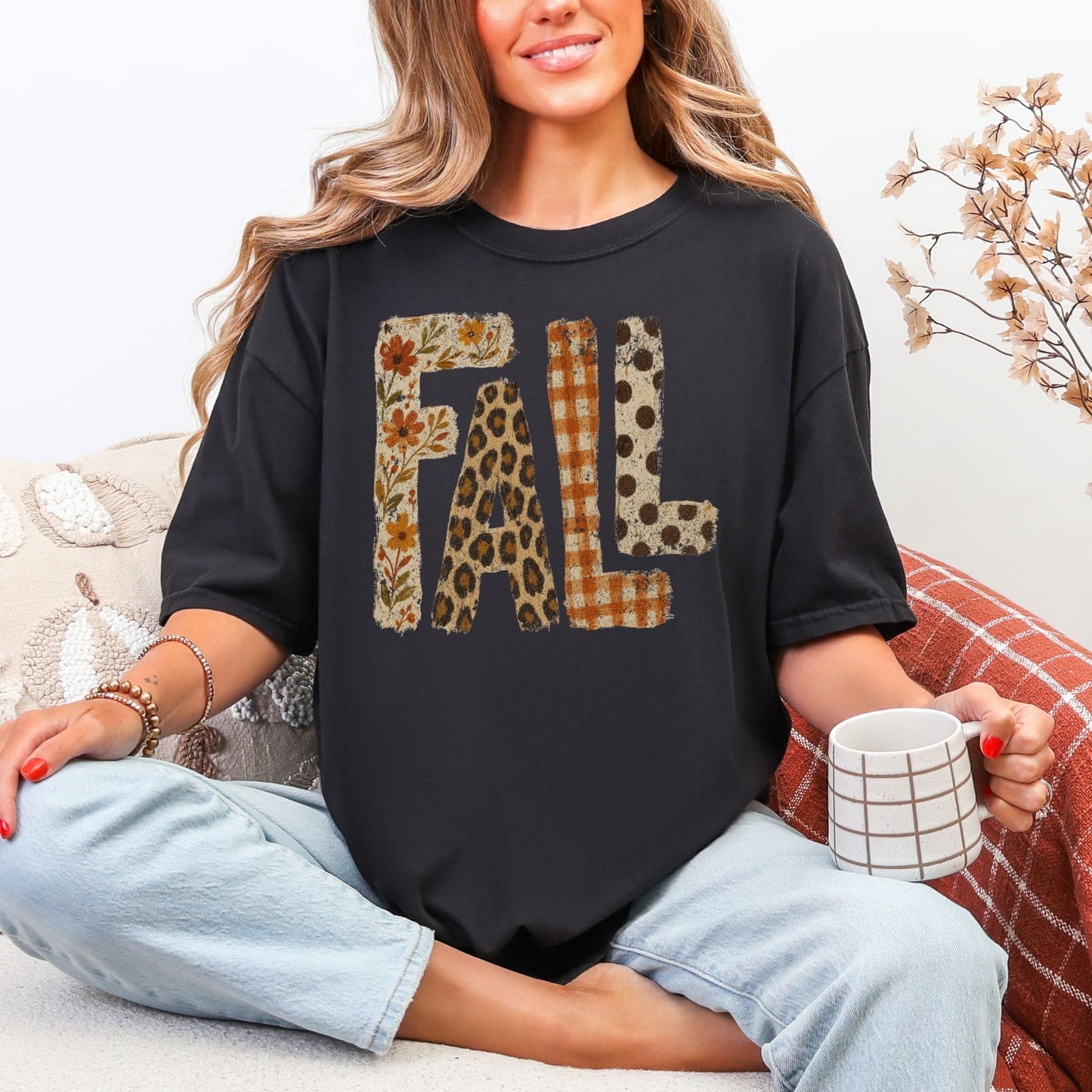 Model wearing a Comfort Colors® 1717 short sleeve t-shirt in black featuring large distressed “FALL” lettering filled with autumn floral, leopard print, orange gingham plaid, and brown polka dot patterns.