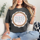 “Embroidery Hoop Home Body" graphic on dark charcoal gray (pepper) t-shirt.”