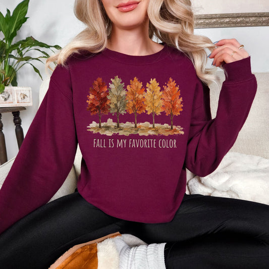 Model wearing a Gildan 18000 Sweatshirt in deep red (maroon) featuring a row of five autumn trees in red, green, orange, and golden yellow with the words “Fall Is My Favorite Color.”