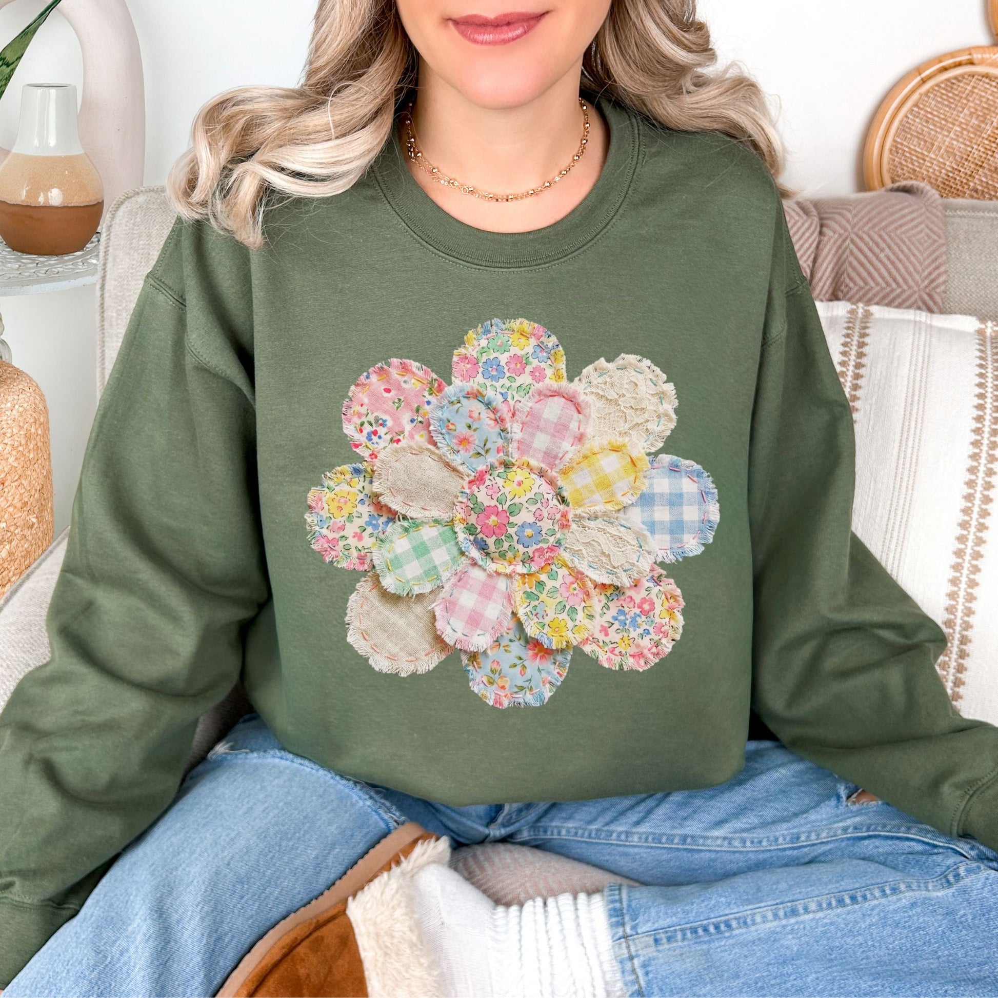 Model is wearing a Gildan 18000 in muted olive green (military green) featuring a faux patchwork flower with pastel floral prints, gingham patterns, and fabric-style textures.