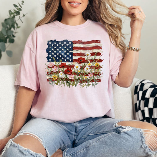 Model is wearing a Comfort Colors 1717 t-shirt in soft pink (blossom) a faux painted American flag design with textured brushstroke details and colorful wildflowers blooming across the bottom.