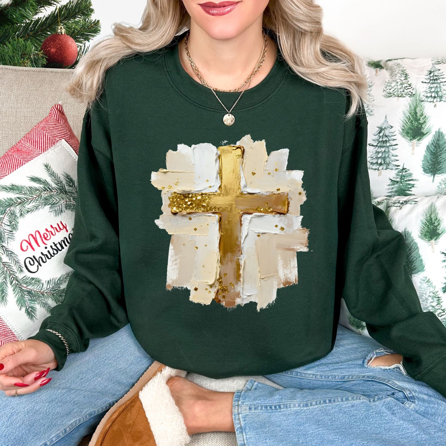 Model wearing a Gildan 18000 crewneck sweatshirt in dark forest green featuring a gold Christian cross surrounded by layered cream, white, and beige faux painted brushstrokes with scattered gold-colored accents.