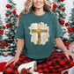 Model wearing a Comfort Colors 1717 T-Shirt in muted blue-green (blue spruce) featuring a gold Christian cross surrounded by layered cream, white, and beige faux painted brushstrokes with scattered gold-colored accents.