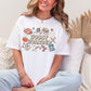 Model wearing a Comfort Colors 1717 t-shirt in bright white (white) color featuring illustrations of hobbies such as blankets, watering can, books and painting supplies with the words "Hobby Hoarder" in the middle in a bubble type font.”
