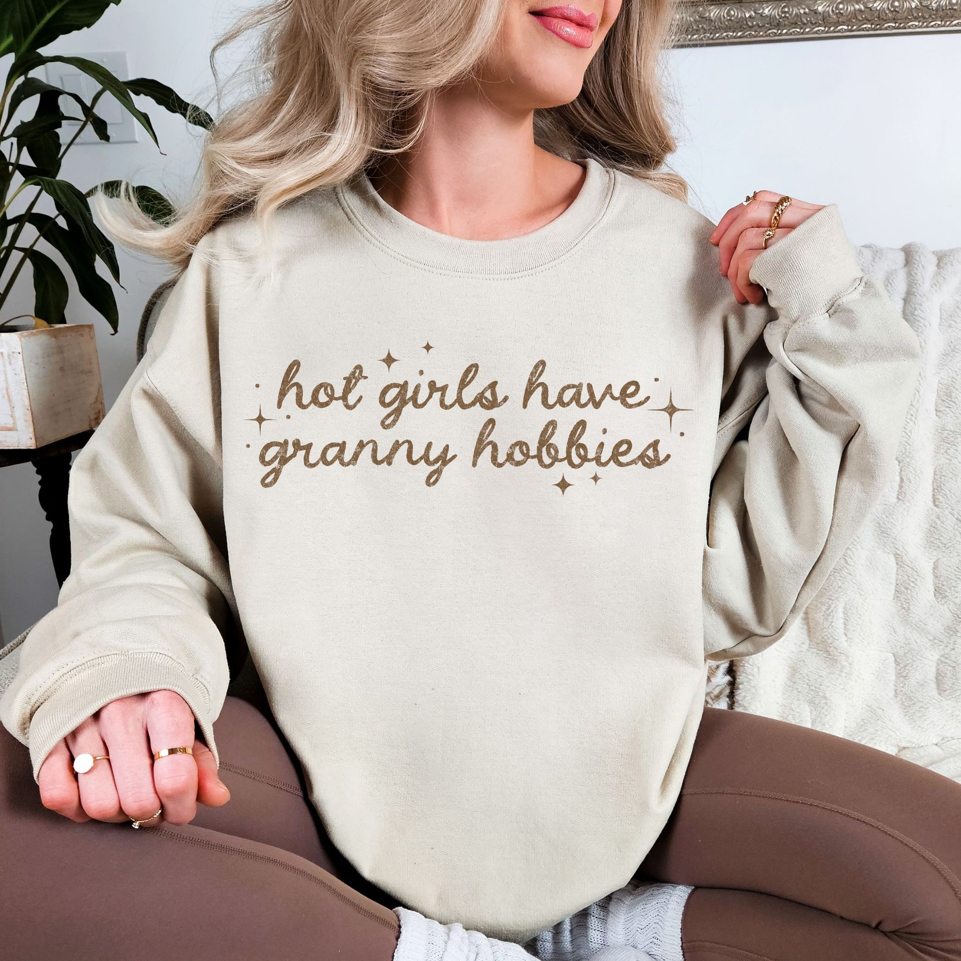 "Hot Girls Have Granny Hobbies" on a Gildan 18000 sweatshirt on light beige (sand) featuring a brown script typography.