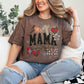 Model is wearing a Comfort Colors t-shirt in deep brown (espresso) featuring the word “mama” in a faux patchwork and embroidery style with leopard print, plaid hearts, stars, and bow accents.