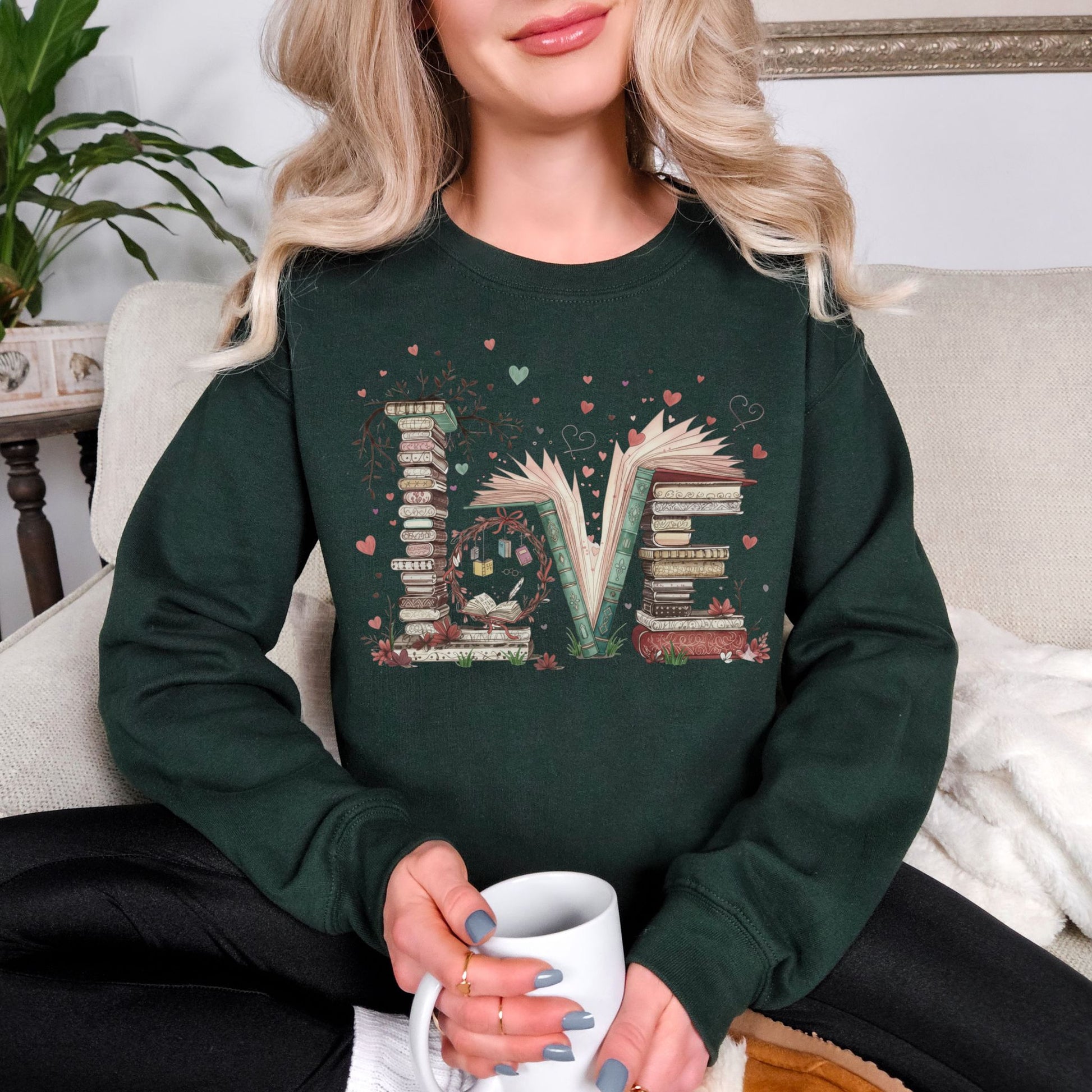 Model wearing a Gildan 18000 sweatshirt in deep forest green (forest green) featuring a whimsical stacked book graphic that spell the word ‘Love’. Along with tiny heart and branch accents.