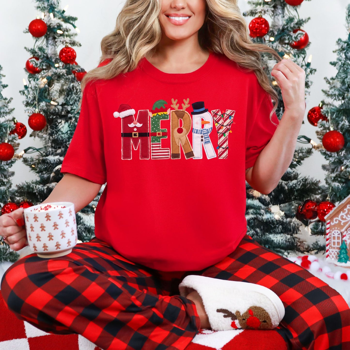 Model wearing a Comfort Colors® 1717 short-sleeve t-shirt in bright red (Red) featuring the word “MERRY” in multicolored Christmas letters with faux felt and stitching details, including Santa, an elf, a reindeer, a snowman, and Christmas lights.