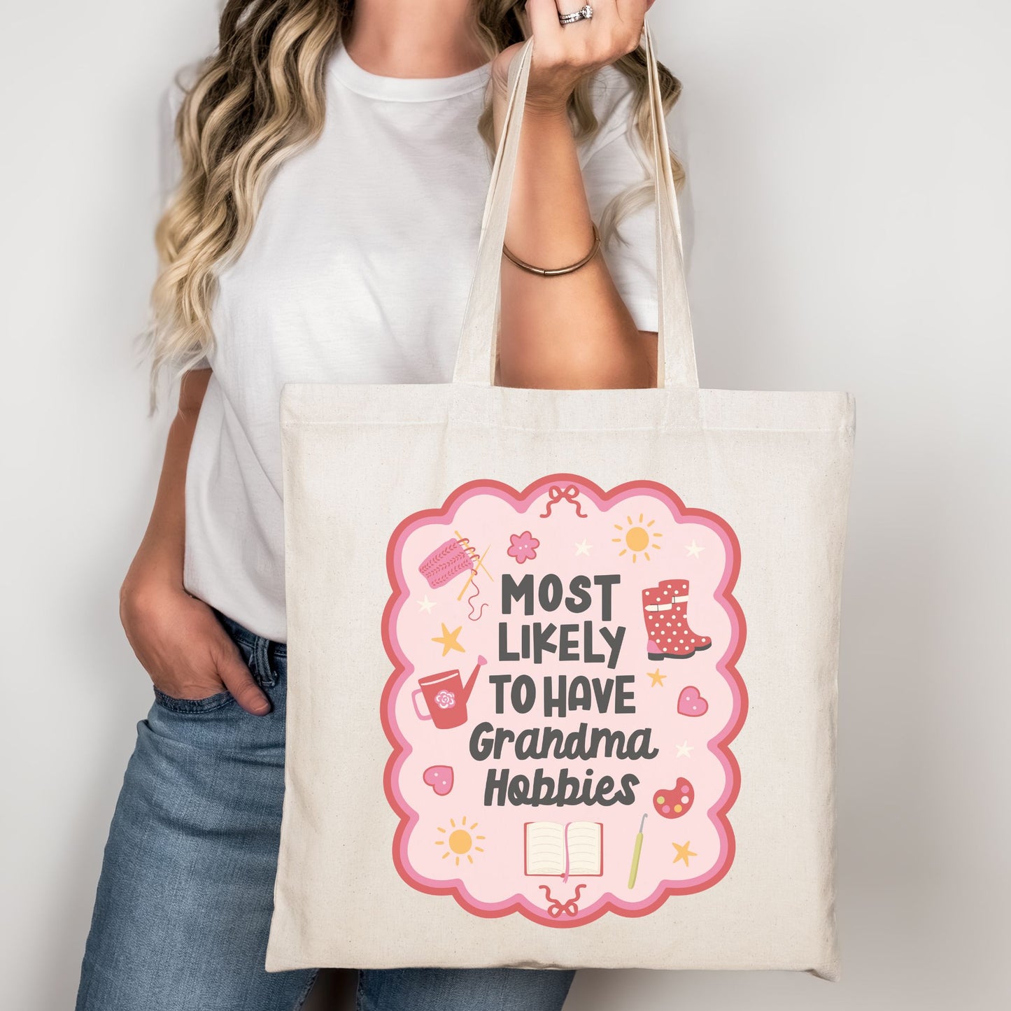 Model holding a natural canvas tote bag with "Most Likely to Have Grandma Hobbies" graphic.