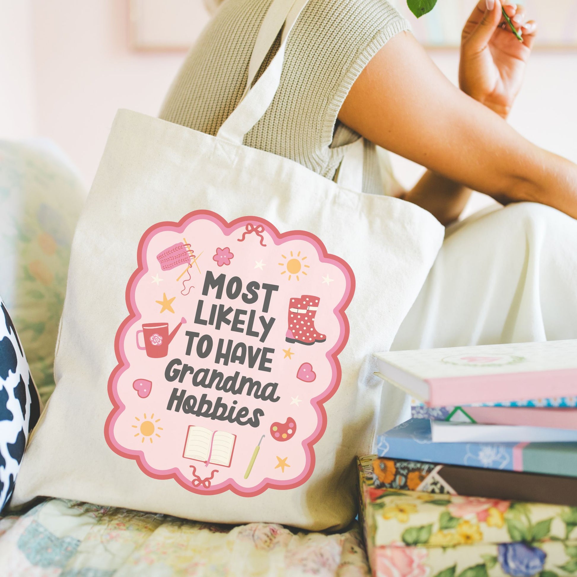 Natural Canvas Tote bag with "Most Likely to Have Grandma Hobbies" design held by a model sitting next to some books. 