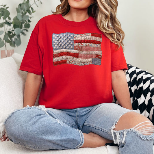 Model is wearing a Comfort Colors 1717 T-Shirt in bright red (red) featuring a faux patchwork American flag design with stars, stripes, gingham, floral prints, and fabric-style textures.
