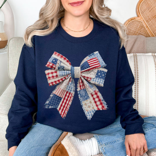 Model wearing a Gildan 18000 sweatshirt in a dark blue (navy) color featuring a patriotic bow in a faux patchwork style with red, white, and blue fabric patterns and lace details.