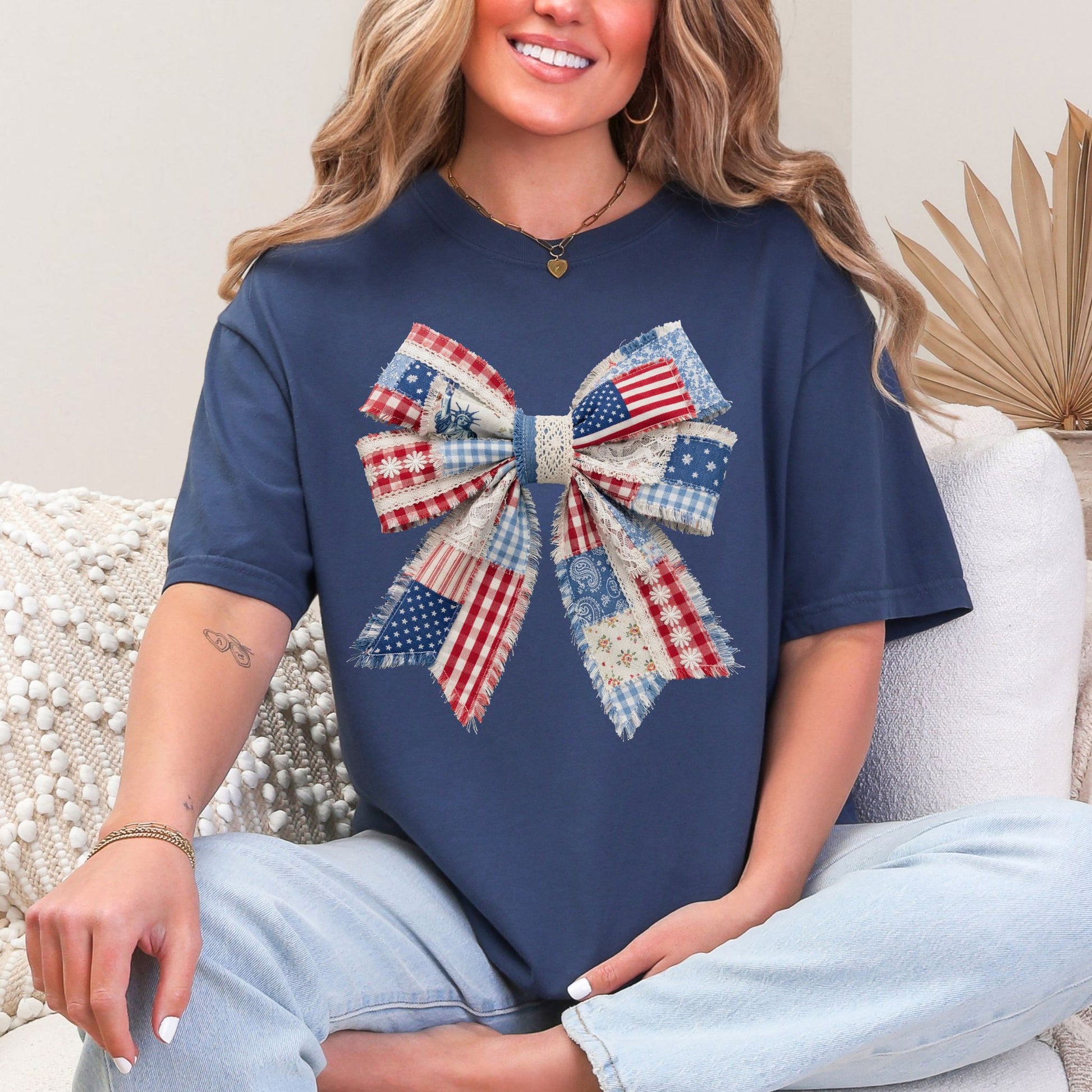 Model wearing a Comfort Colors 1717 t-shirt in a deep navy blue (navy) color featuring a patriotic bow in a faux patchwork style with red, white, and blue fabric patterns and lace details.