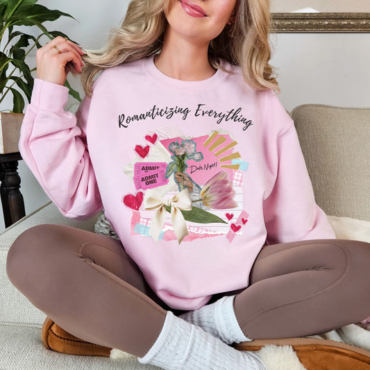 Model is wearing a Gildan 18000 sweatshirt in soft pale pink (light pink) featuring a Scrapbook-style collage graphic with soft pink (blush pink) paper, red (petal pink) hearts, a cream (soft beige) bow, and a pink (soft peach) tulip. Handwritten text reads “Romanticizing Everything” and “Date Night!” in a cozy junk journaling aesthetic.