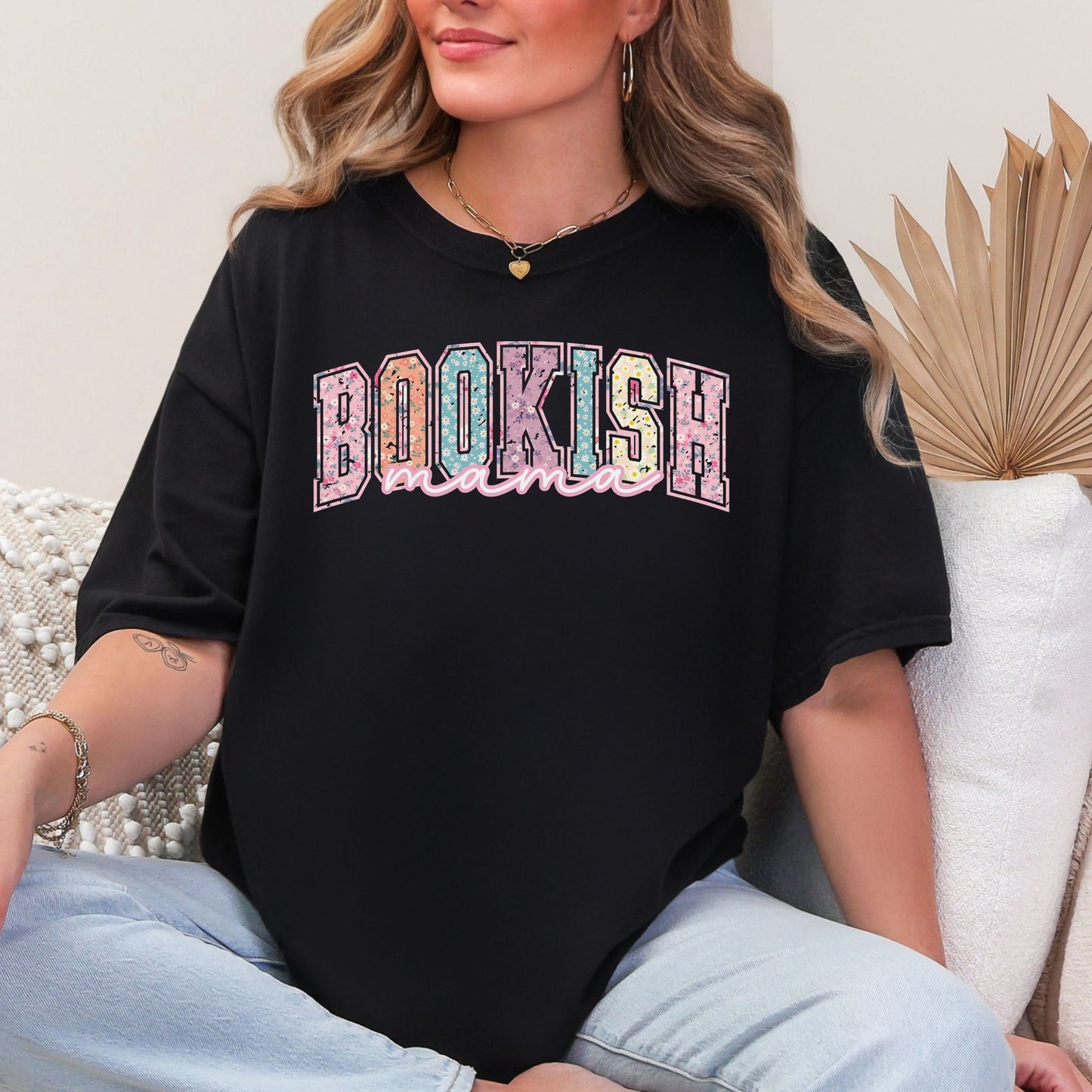 Model is wearing a Comfort Colors 1717 T-shirt in black. The shirt features a graphic design that says, "Bookish mama". "Bookish" are in a varsity letter font filled in with a beautiful pastel spring floral design.