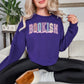 Model is wearing a Gildan 18000 sweatshirt in medium purple (purple). The shirt features a graphic design that says, "Bookish mama". "Bookish" are in a varsity letter font filled in with a beautiful pastel spring floral design.