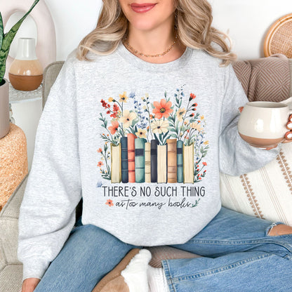 Model wearing a Gildan 18000 sweatshirt in very light gray (ash) featuring books lined up with wildflower florals behind it.  Underneath is the phrase "There's no such thing as too many books" in a mix of script and cursive fonts. 