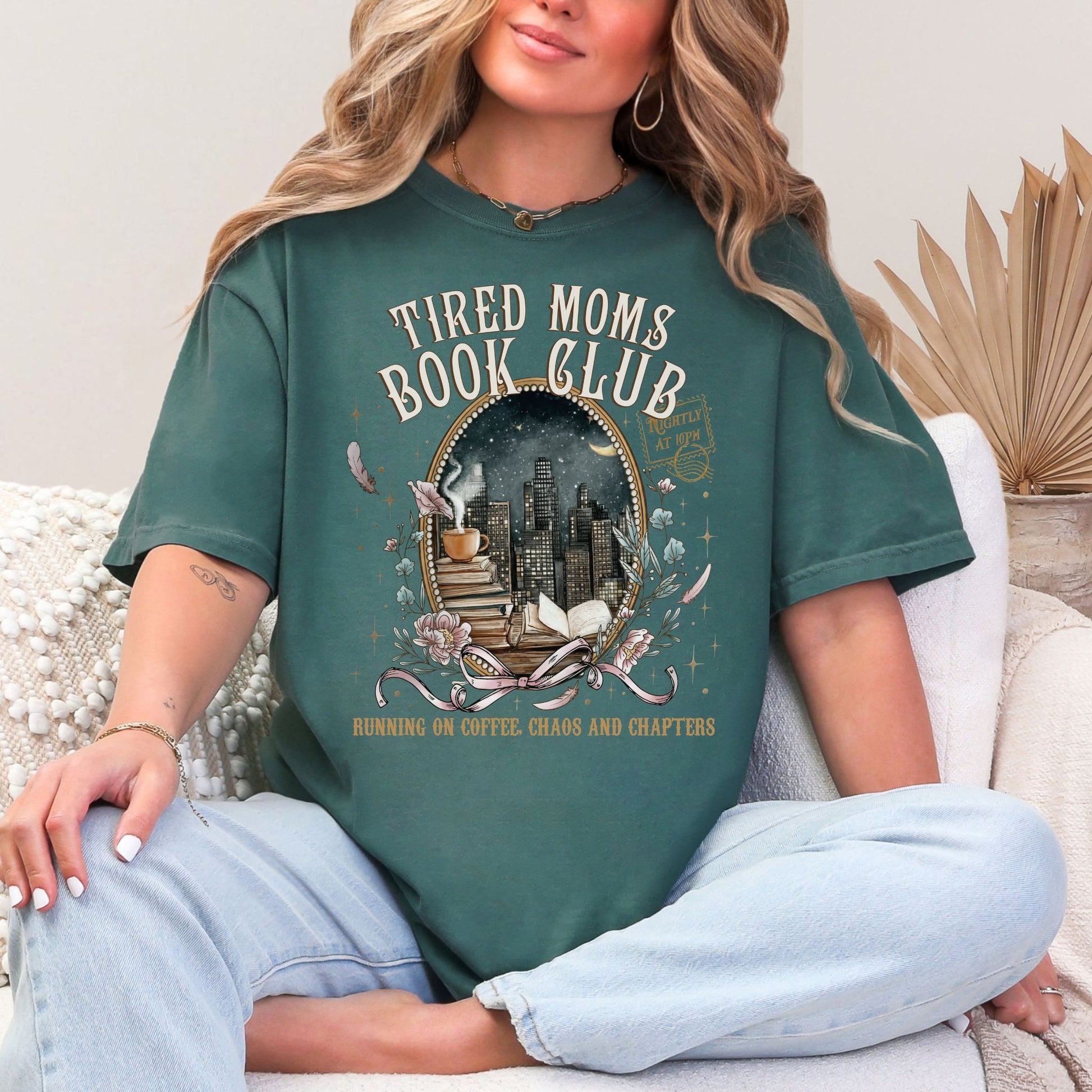 "Tired Moms Book Club" graphic on muted blue-green (blue spruce) t-shirt.