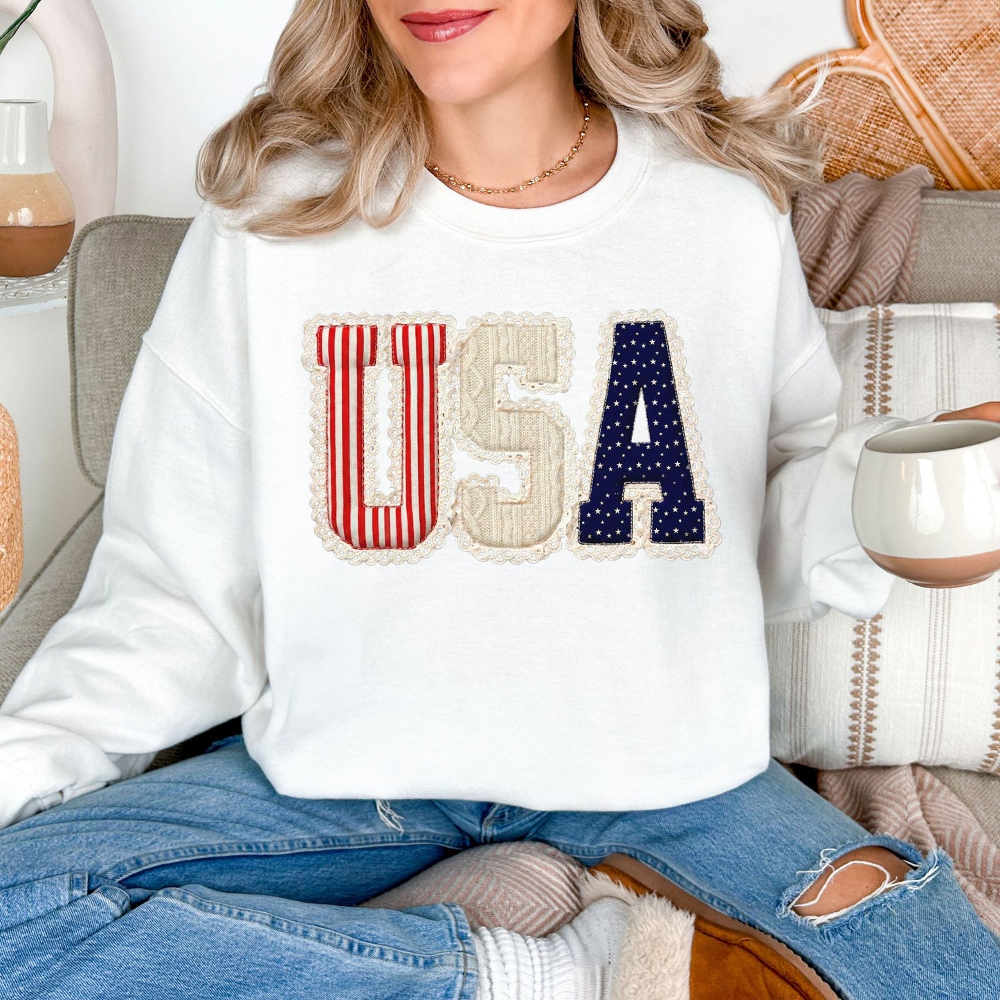 Model wearing a Gildan 18000 sweatshirt in very white (white) with a patriotic “USA” design featuring striped, knit-style, and star patterns accented with lace-style borders in a faux embroidery style.